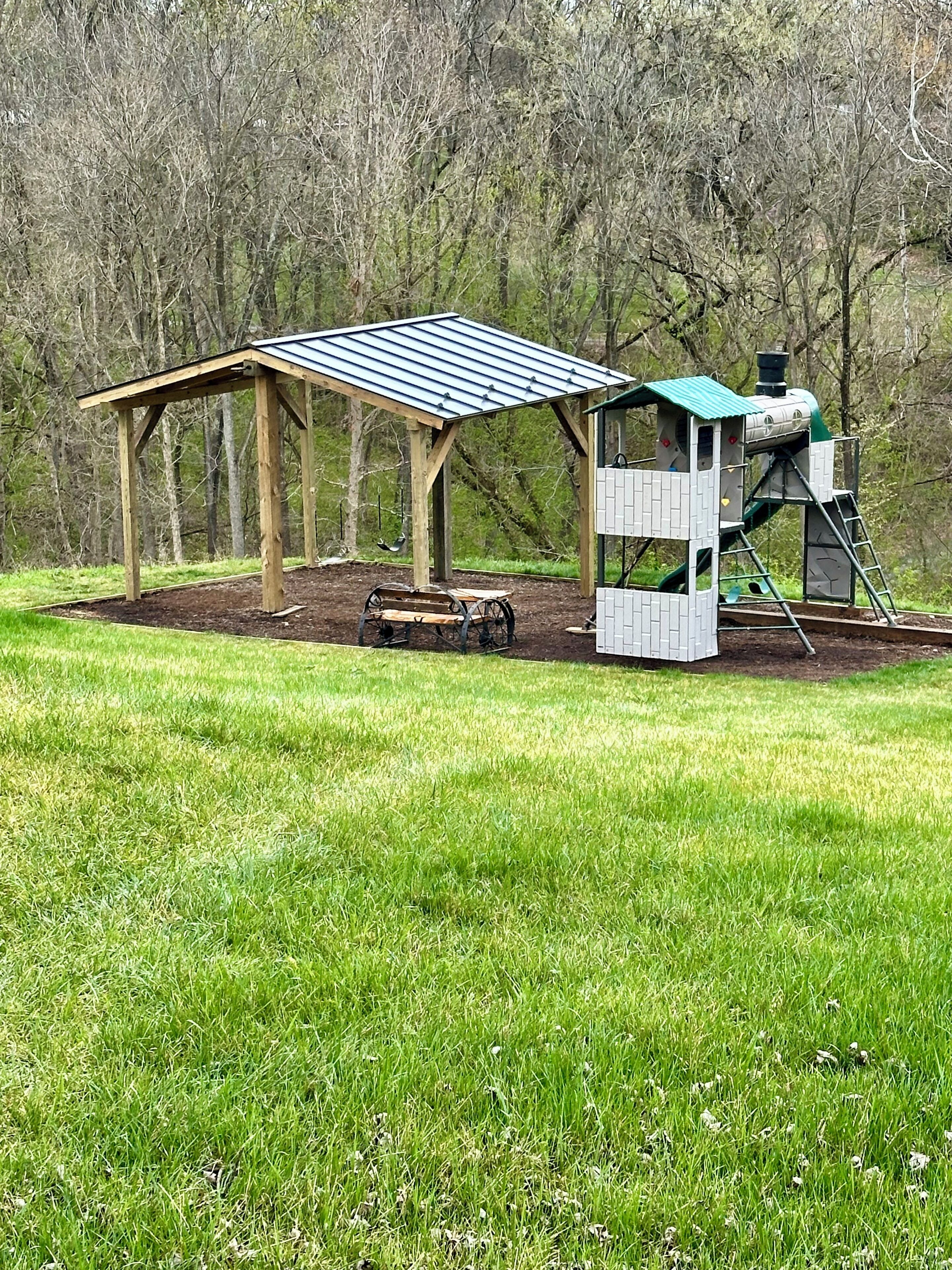 A wooden pavilion with a metal roof and a small play structure.