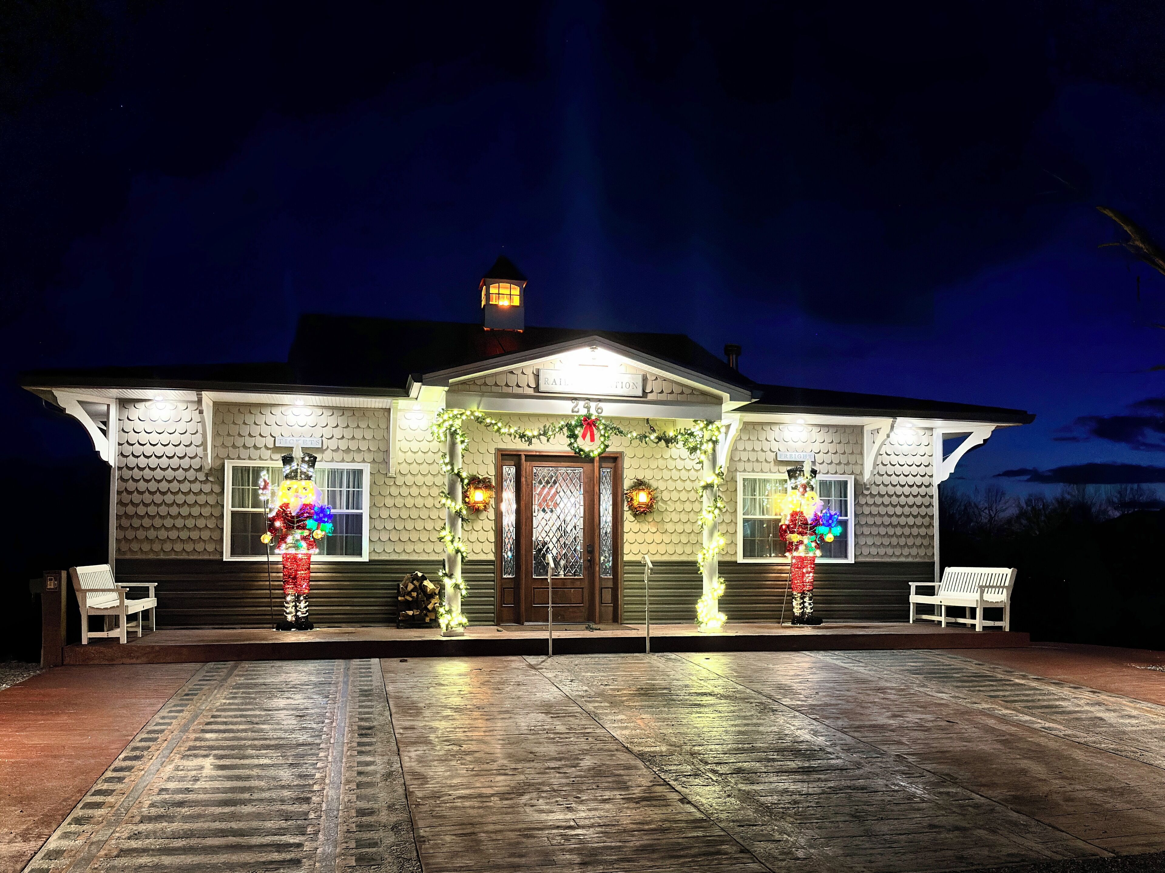A house with a tiled exterior, a front porch with benches, and a lit front door.