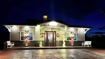 A house with a tiled exterior, a front porch with benches, and a lit front door.