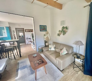 A living room with a sofa, coffee table, and lamp. There is a dining area with chairs and a table. - "Le Patio" with Sea View, Wi-Fi, and Air Conditioning (Bormes-les-Mimosas)