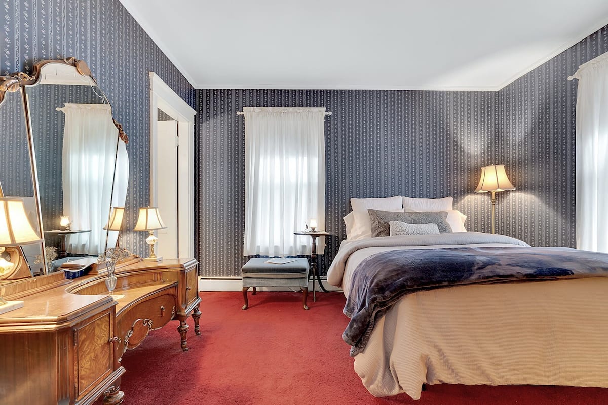 A bedroom with a large bed, a dresser with a mirror, and a nightstand with a lamp.