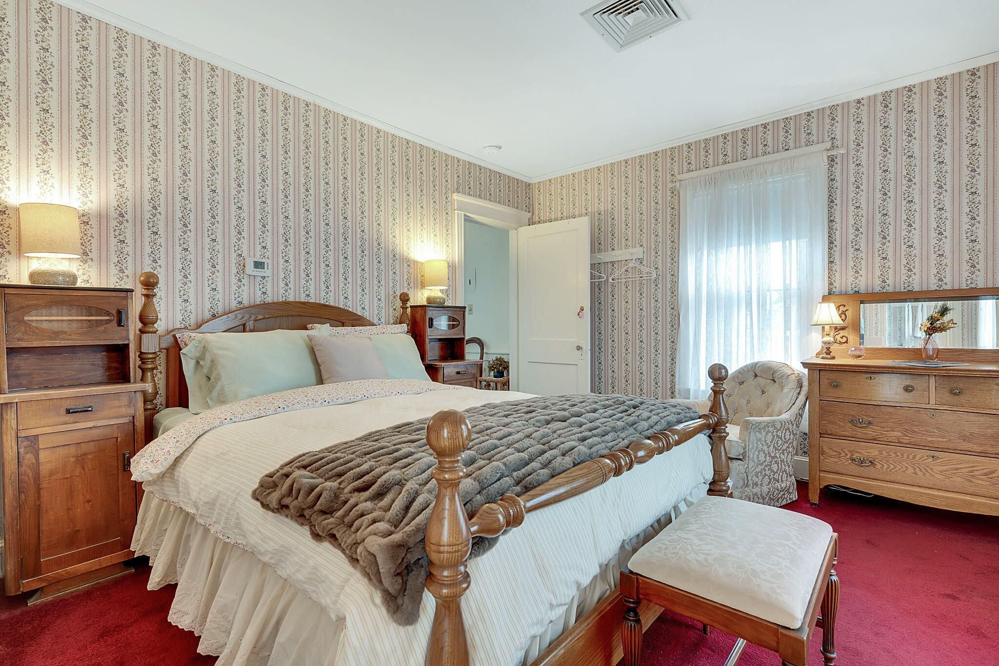 A traditional bedroom with a wooden bed, a wooden dresser, a chair, and a nightstand.