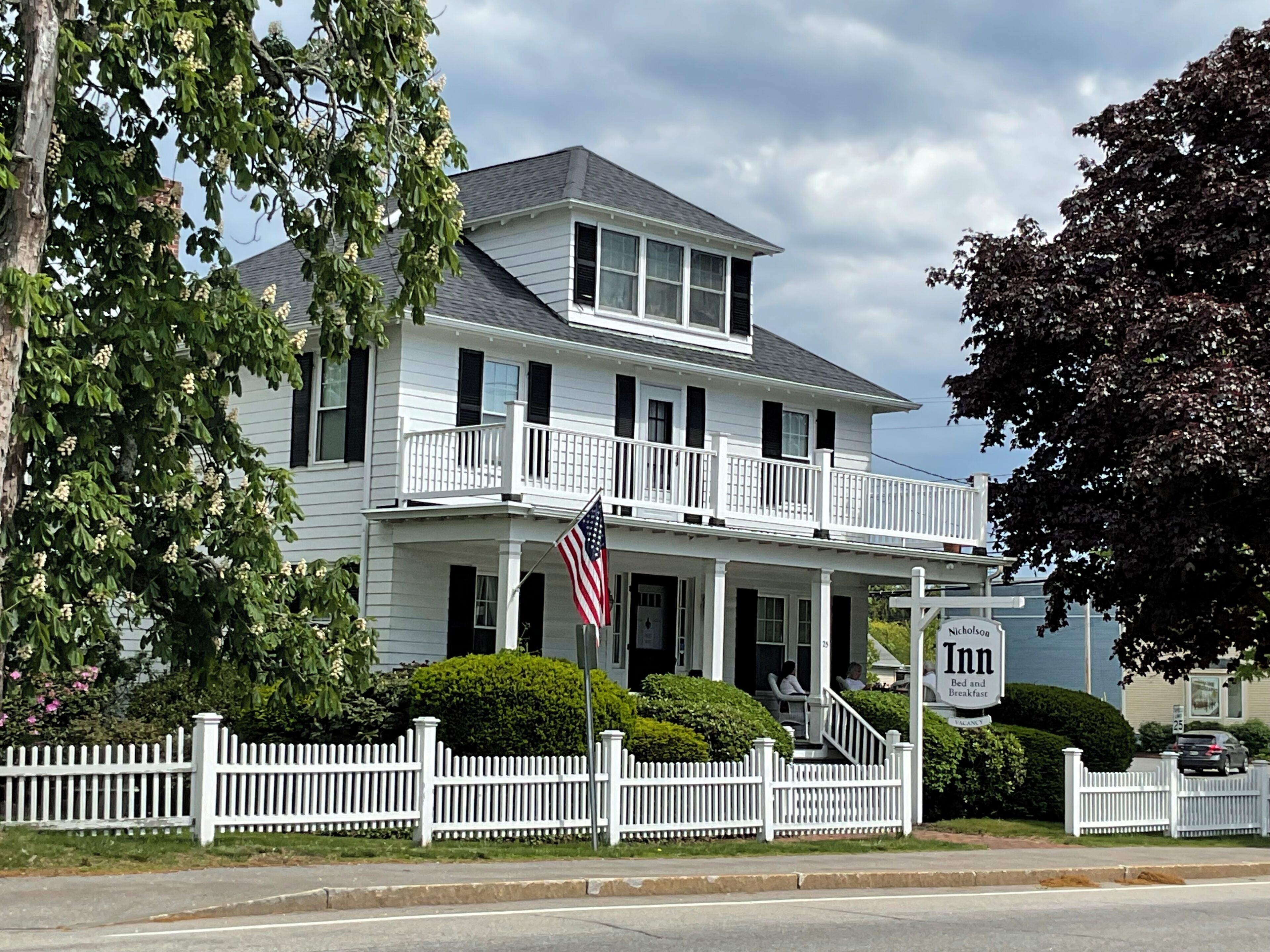 A two-story white building with a balcony, a flag, and a sign for 'Nicholson Inn Bed and Breakfast.'