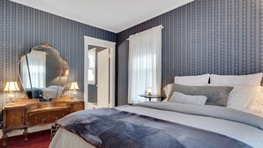 A bedroom with a large bed, a dresser with a mirror, and a nightstand with a lamp. - The Nicholson Inn (Freeport)