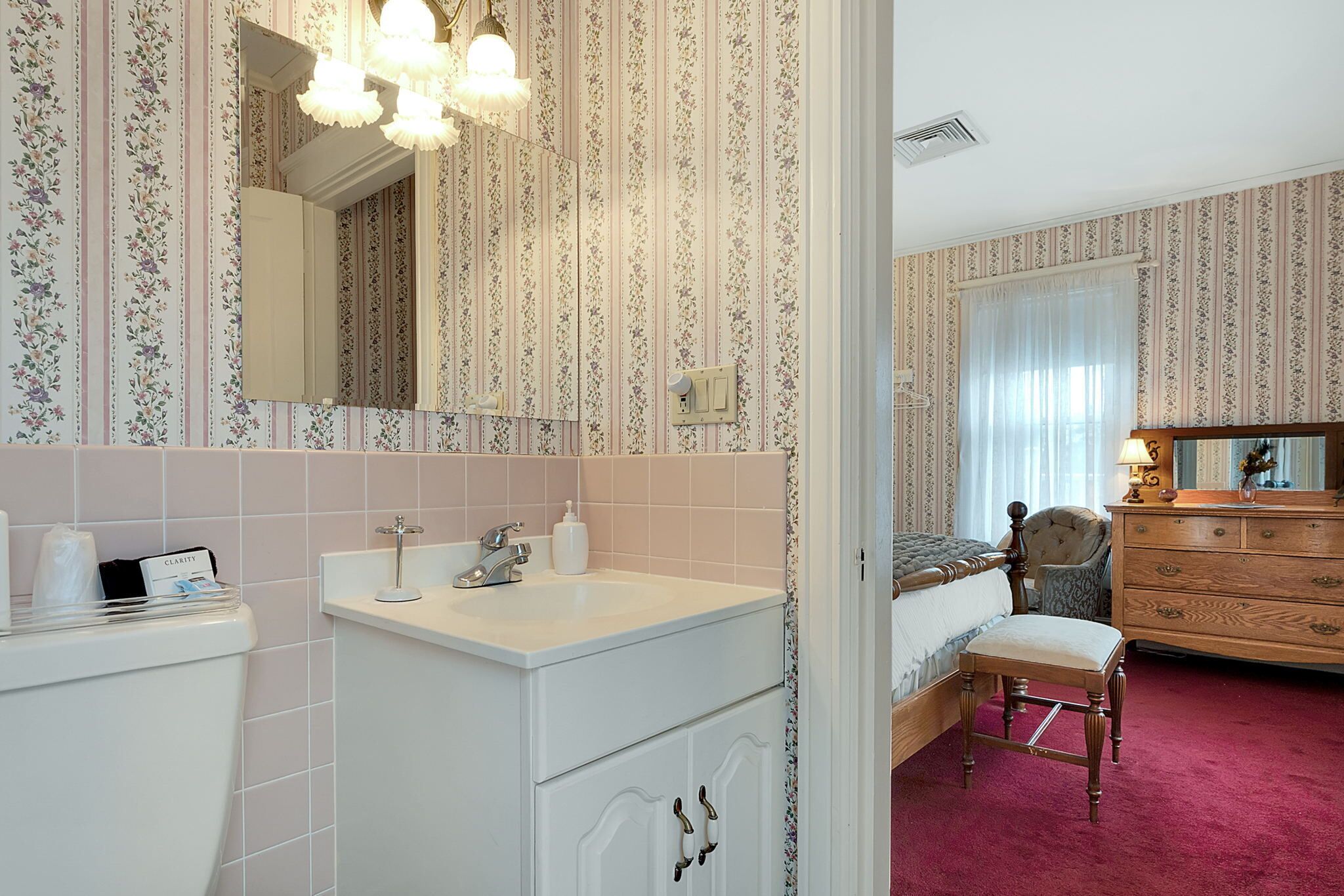 A hotel room with a bathroom, a bed, a wooden dresser, and a chair.