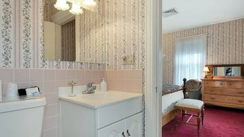 A hotel room with a bathroom, a bed, a wooden dresser, and a chair.