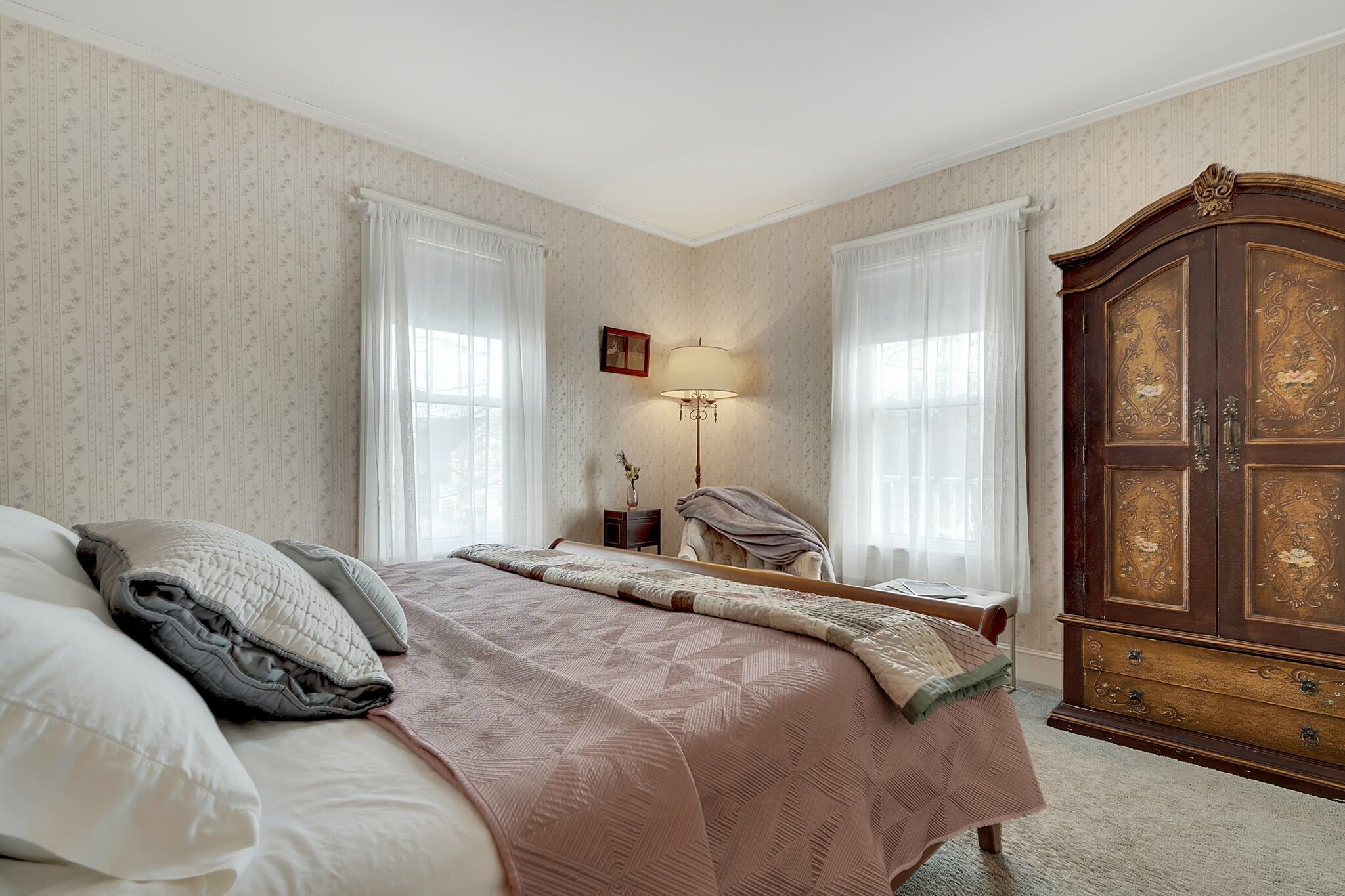 A bedroom with a bed, a nightstand, a lamp, and a wooden wardrobe.