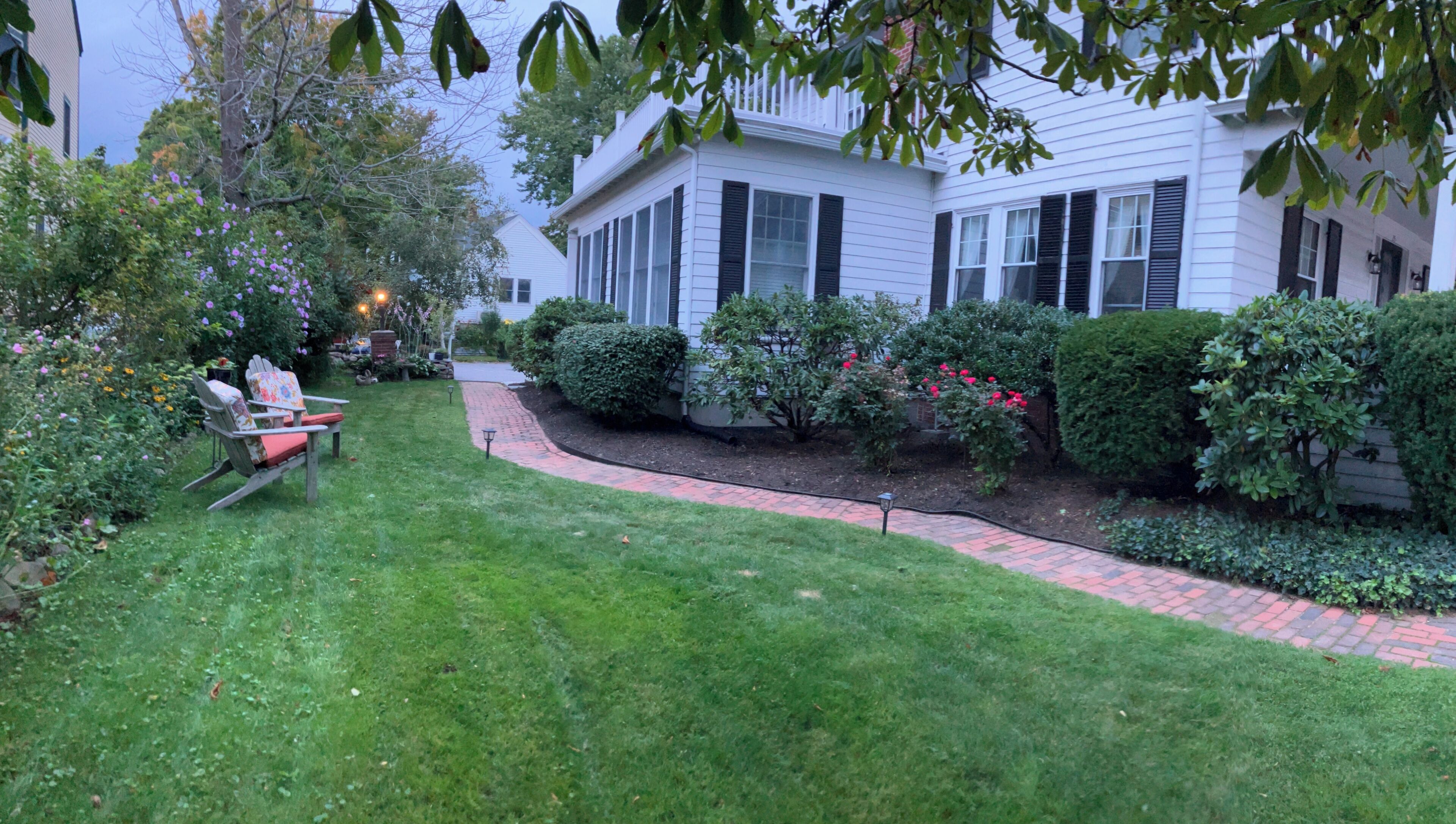 A residential house with a well-maintained lawn, a brick pathway, and a garden with various plants and flowers.