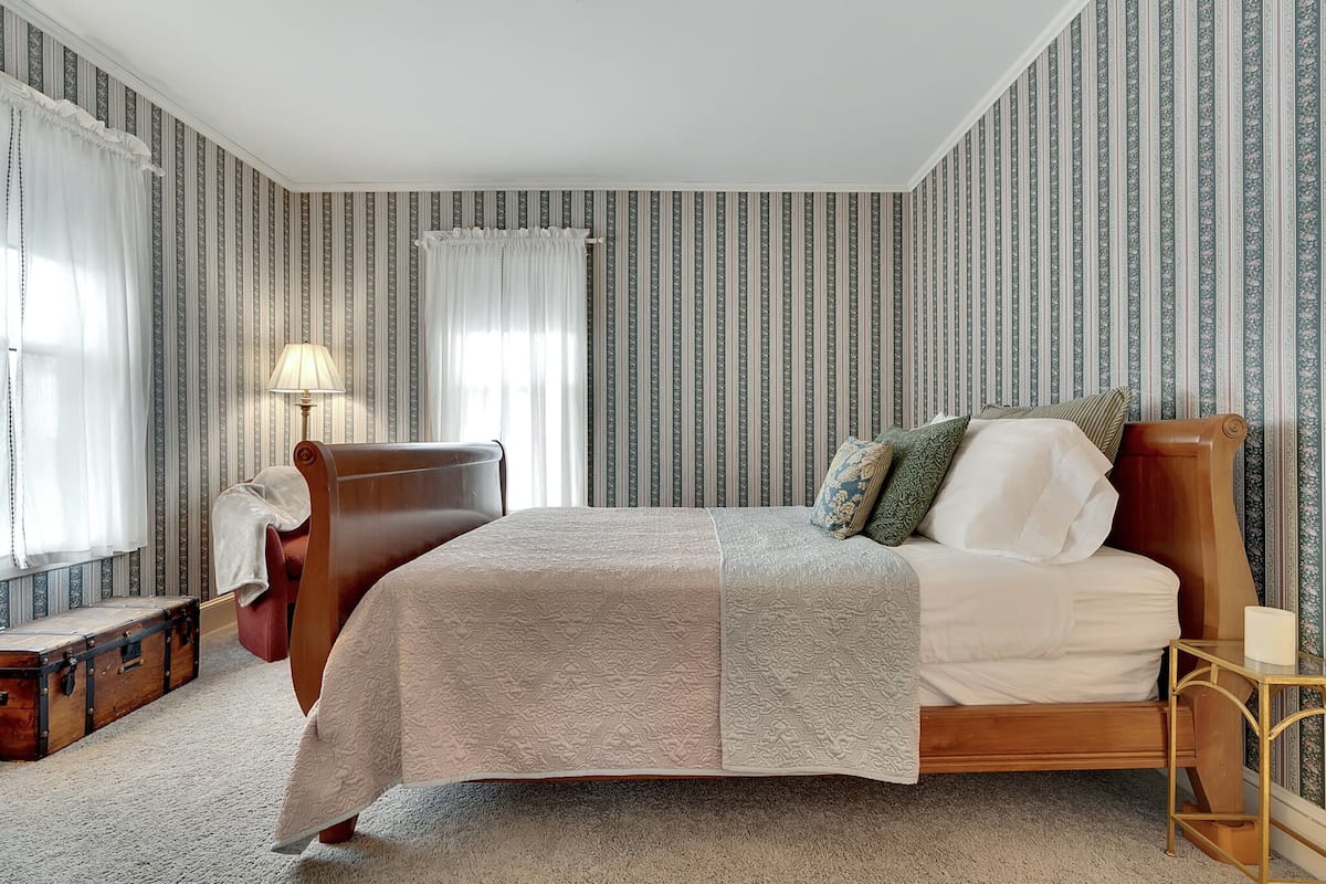 A neatly arranged bedroom with a large bed, a wooden chair, a small table, and a suitcase on the floor.