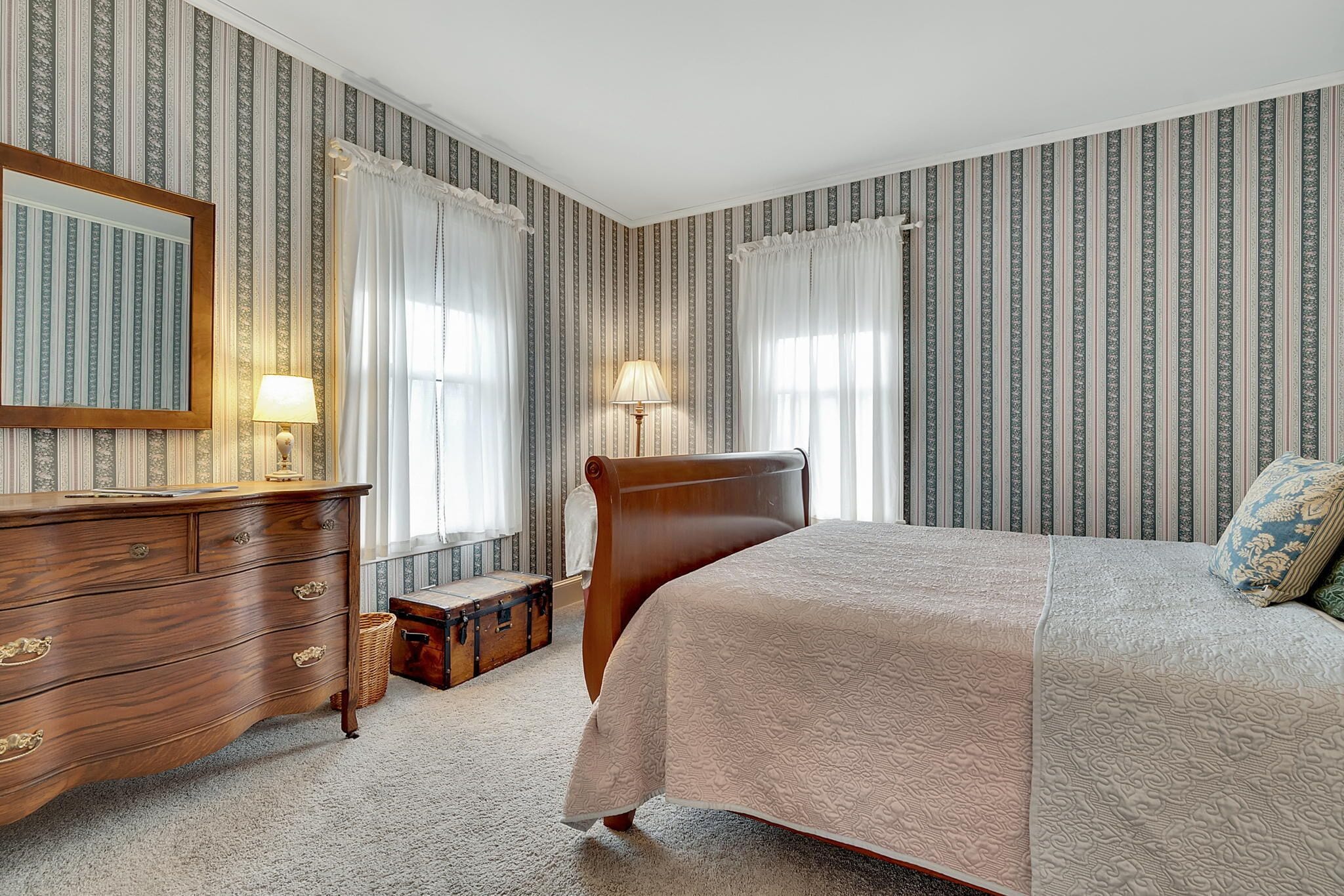 A bedroom with a large bed, a wooden dresser, two lamps, and a mirror.