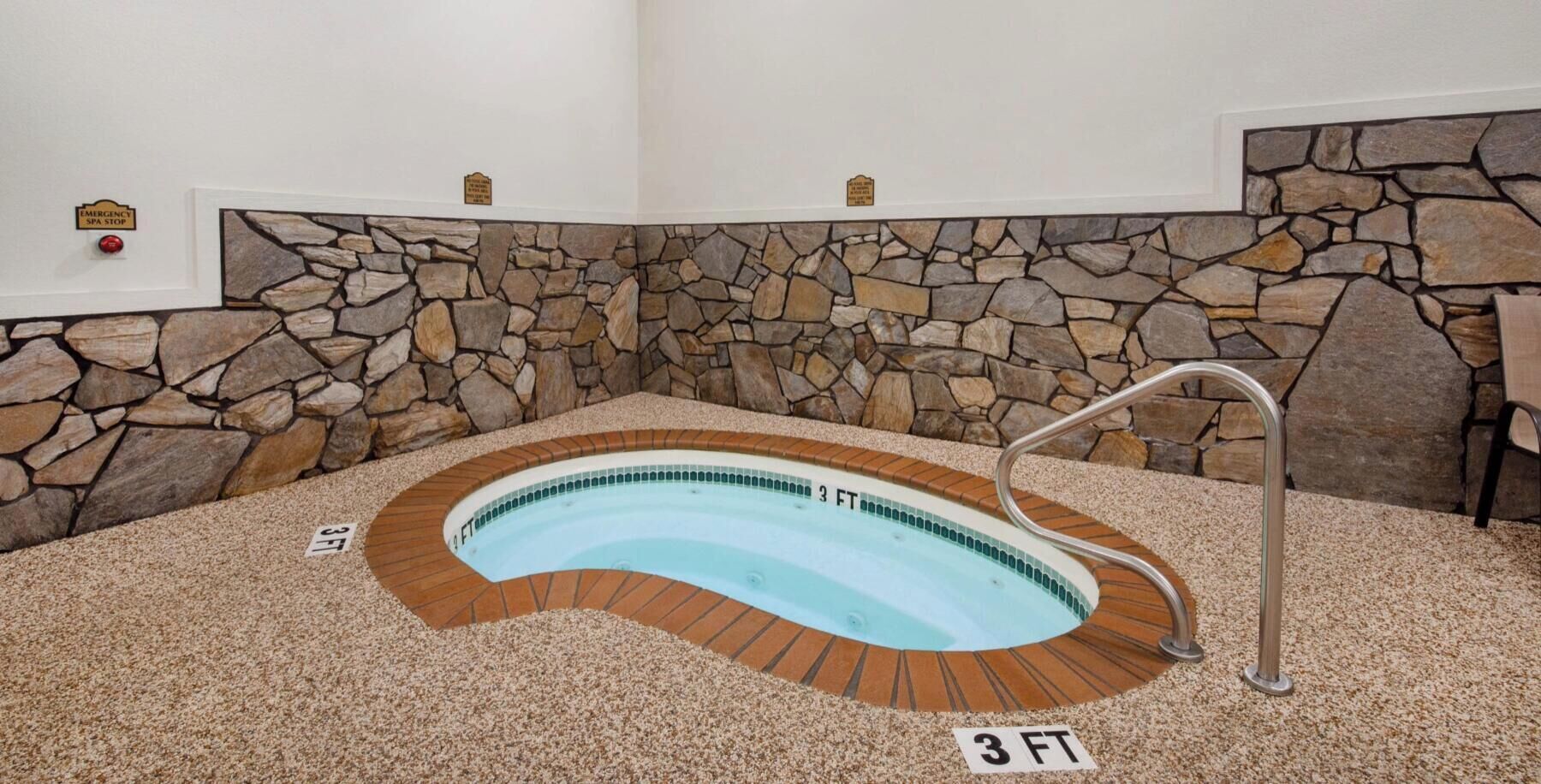 A hot tub with a stone wall backdrop, a metal ladder, and a 3 FT depth marker.