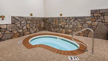A hot tub with a stone wall backdrop, a metal ladder, and a 3 FT depth marker.