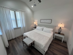 A bedroom with a bed, two bedside tables, a chair, a ceiling fan, and a window with curtains.