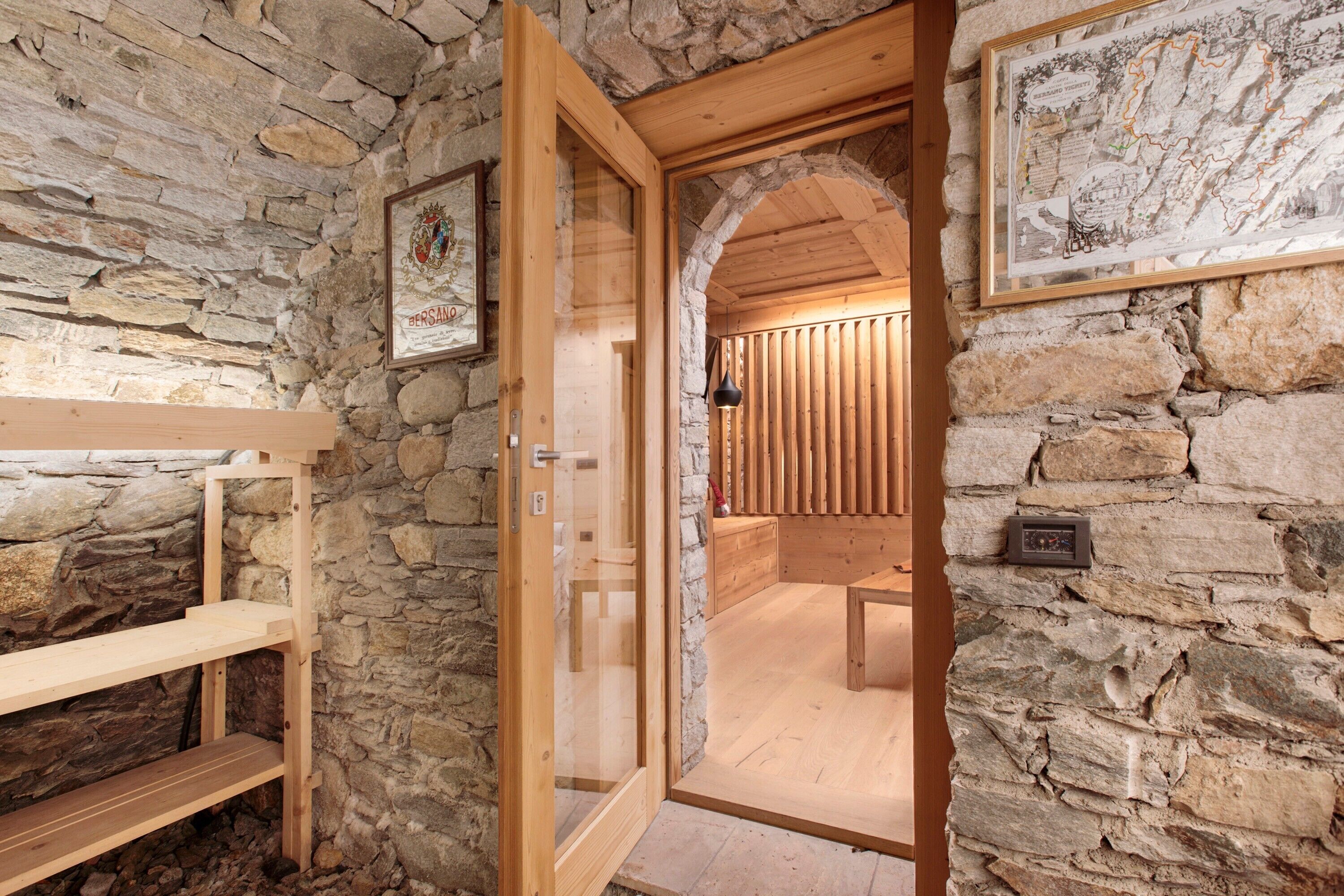 A stone-walled room with a wooden bench, a framed certificate, and a map on the wall.