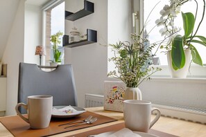 A dining area with a table set for two, a vase with flowers, and a window with plants. - Apartment for 2 people (Heiligenhafen)