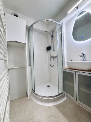 Un baño moderno con ducha de vidrio, lavamanos blanco y espejo.