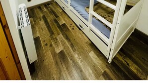 Quarto pequeno e compacto com uma cama beliche, uma janela com cortinas e um radiador.