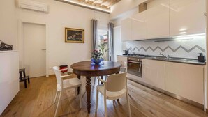Una cuina moderna amb armaris blancs, una taula de menjador de fusta i un forn de mur.