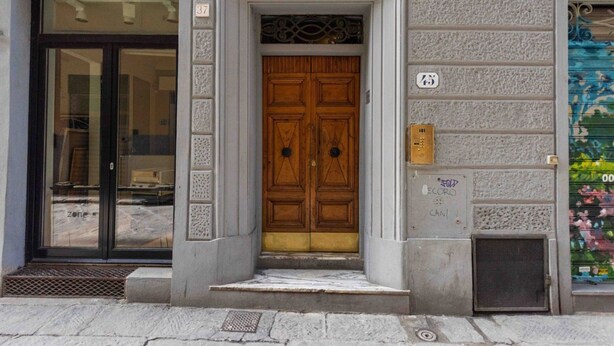 Entrada d'un edifici amb una porta doble de fusta, uns quants escalons i una porta de vidre a l'esquerra.