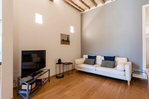 Ein Wohnzimmer mit einem Flachbildfernseher auf einem Glastisch, einem weißen Sofa mit Kissen und einem Gemälde an der Wand.