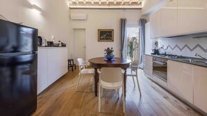 Una cuina moderna amb armaris blancs, un frigorífic negre, una taula de dinar de fusta amb caires blancs i una vista a la ciutat a través d'una finestra.