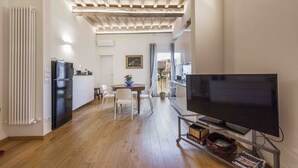 Cuina moderna amb nevera integrada, zona de menjador amb taula i cadires, i un televisor sobre un suport.