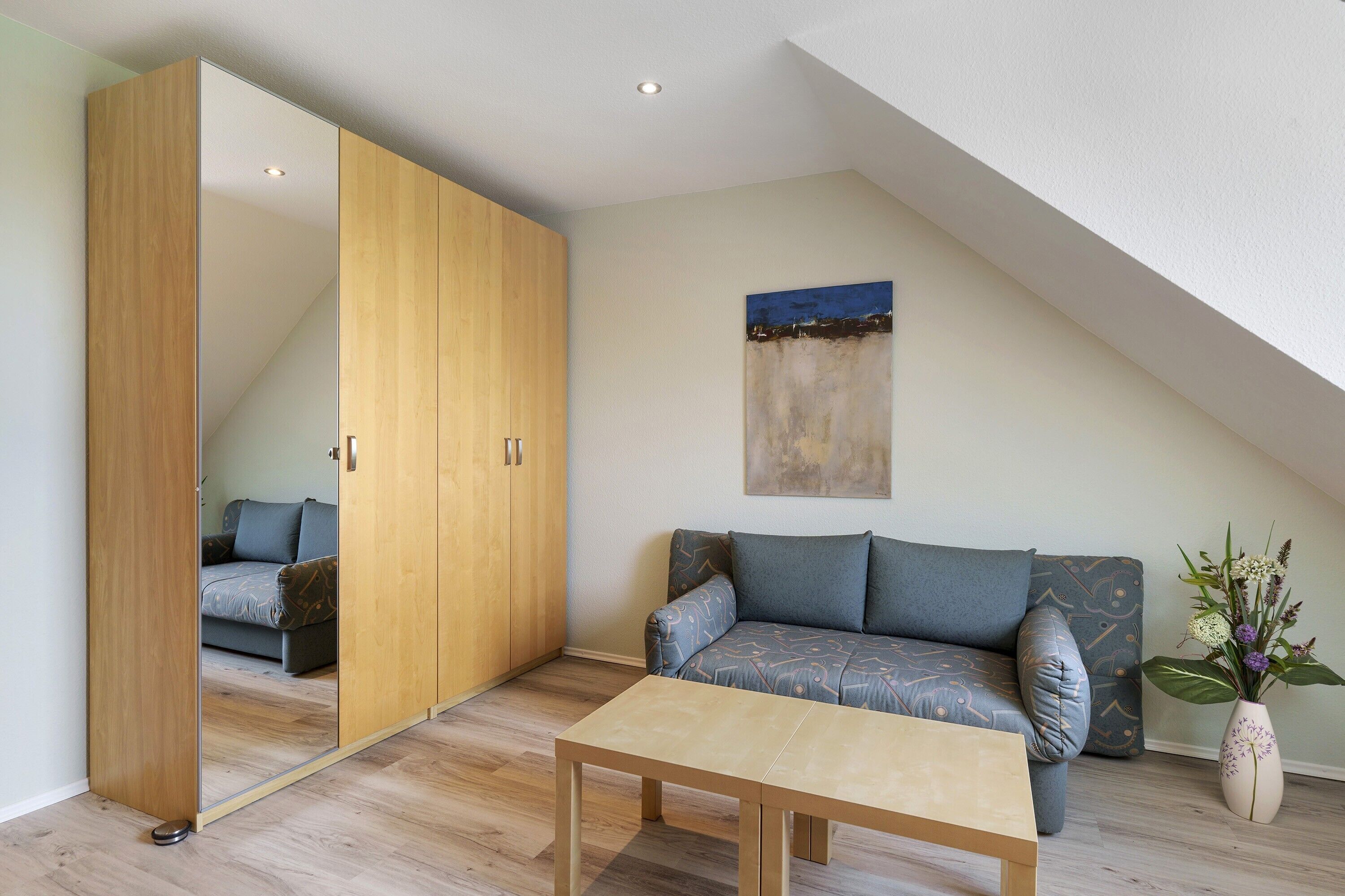 Una habitación moderna con un armario de madera, un sofá, una mesita de centro y un cuadro en la pared.