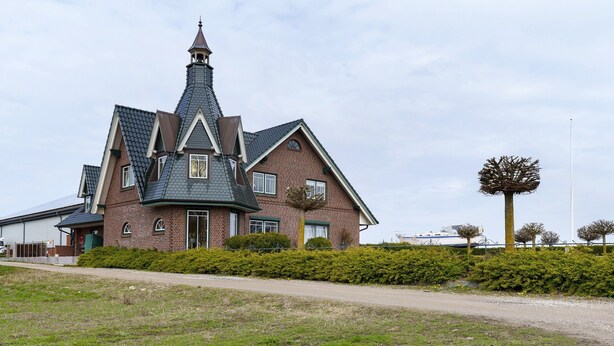 Uma casa grande, de vários andares, com uma torre imponente, um gramado bem cuidado e um céu claro.