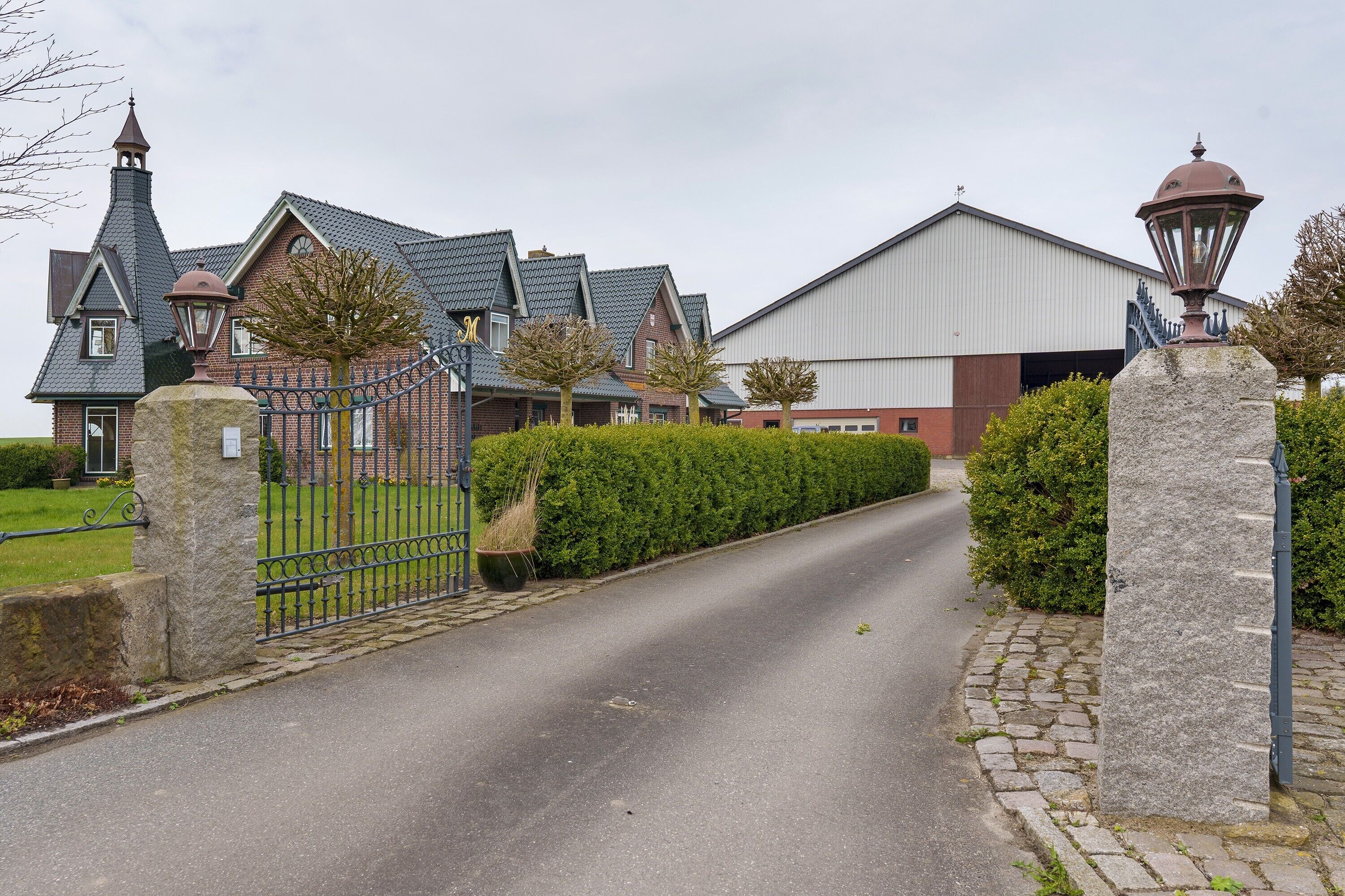 A gated driveway leading to a building with a large industrial structure in the background.