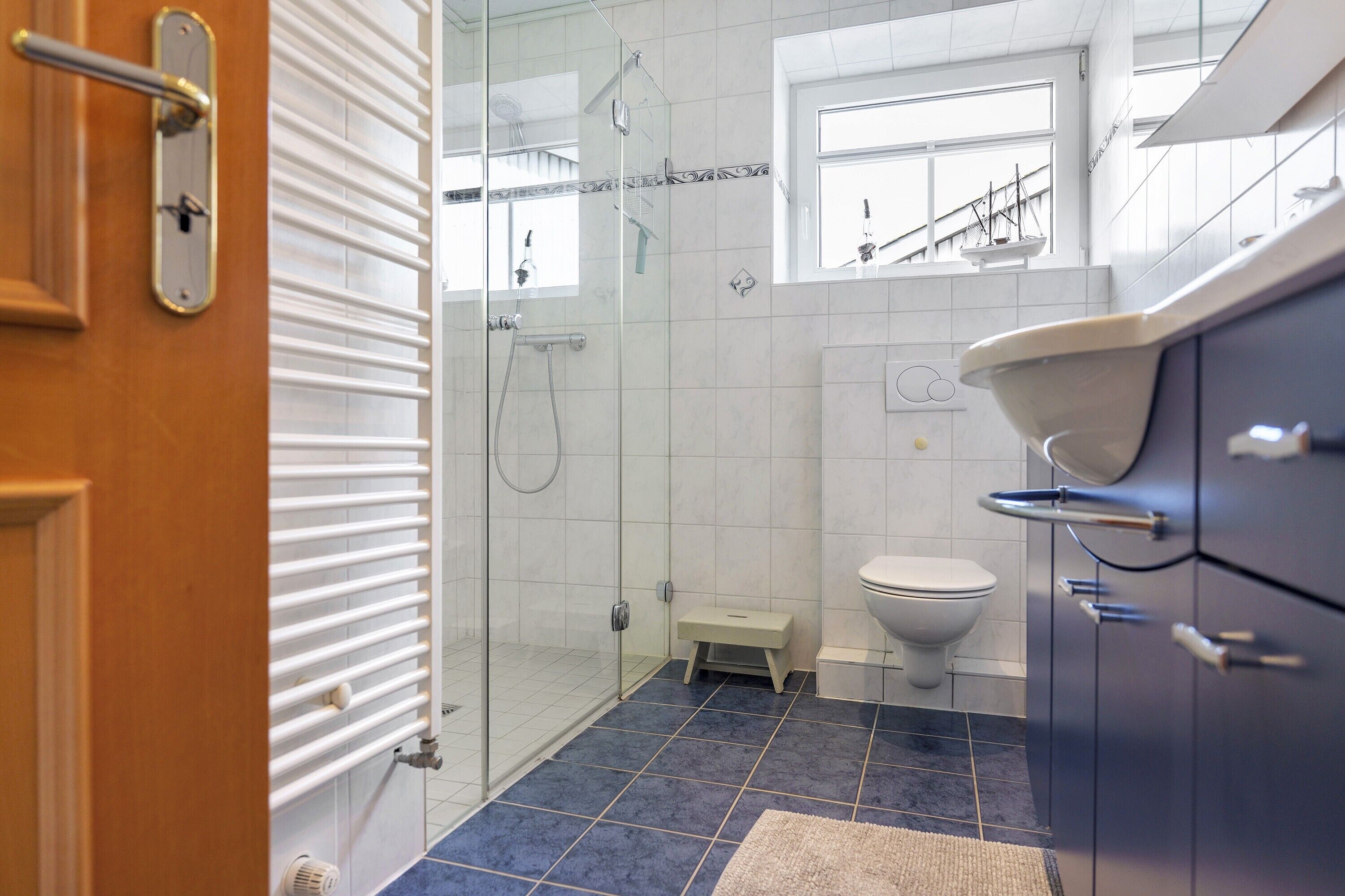 A bathroom with a glass shower enclosure, a toilet, a sink, and a window.