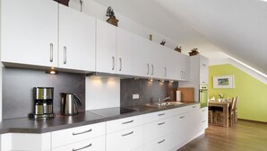 Uma cozinha moderna com armários brancos, eletrodomésticos de aço inoxidável e uma sala de jantar com mesa e cadeiras de madeira.