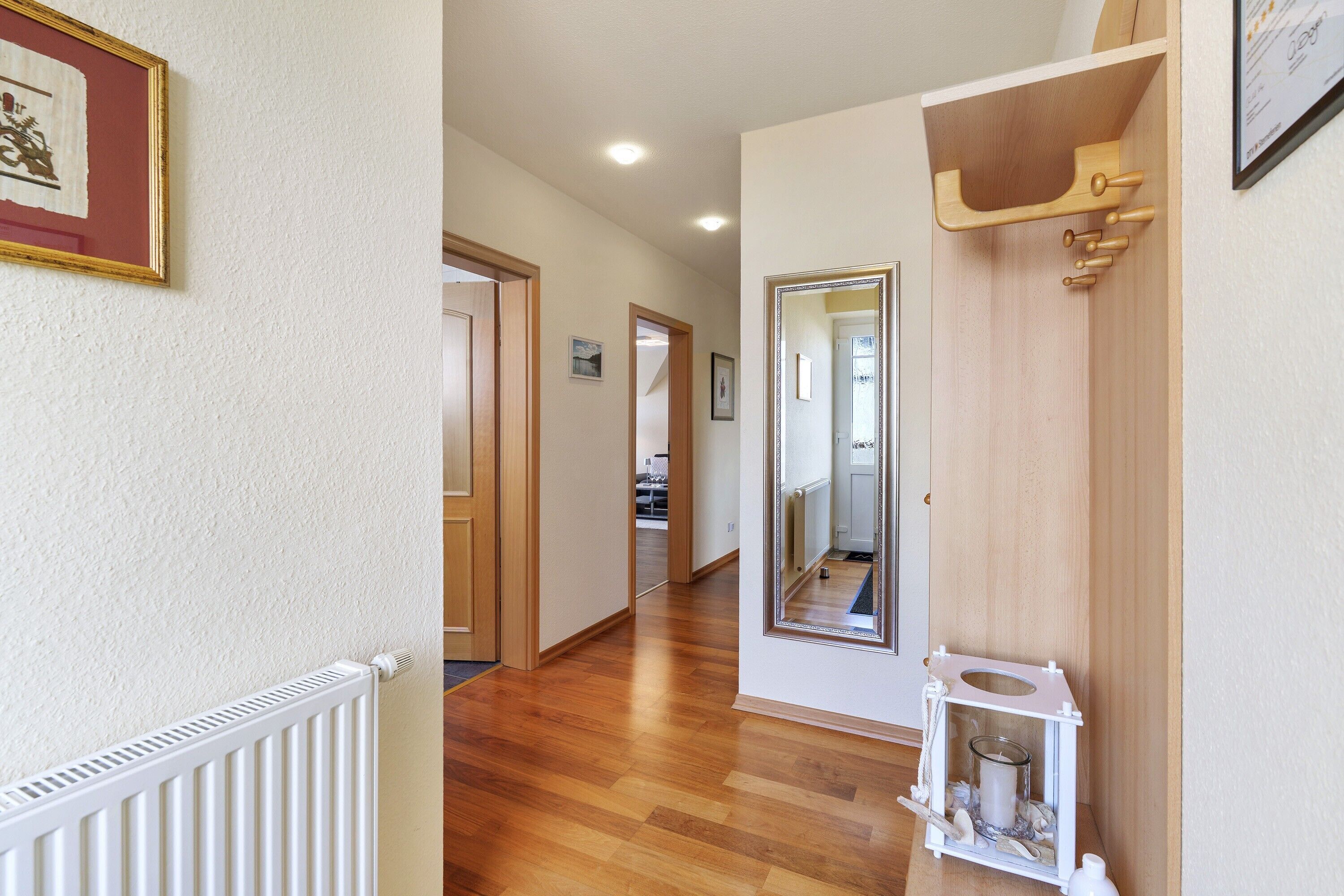 A hallway with wooden flooring, a white radiator, a framed picture, a mirror, and a small white cabinet.