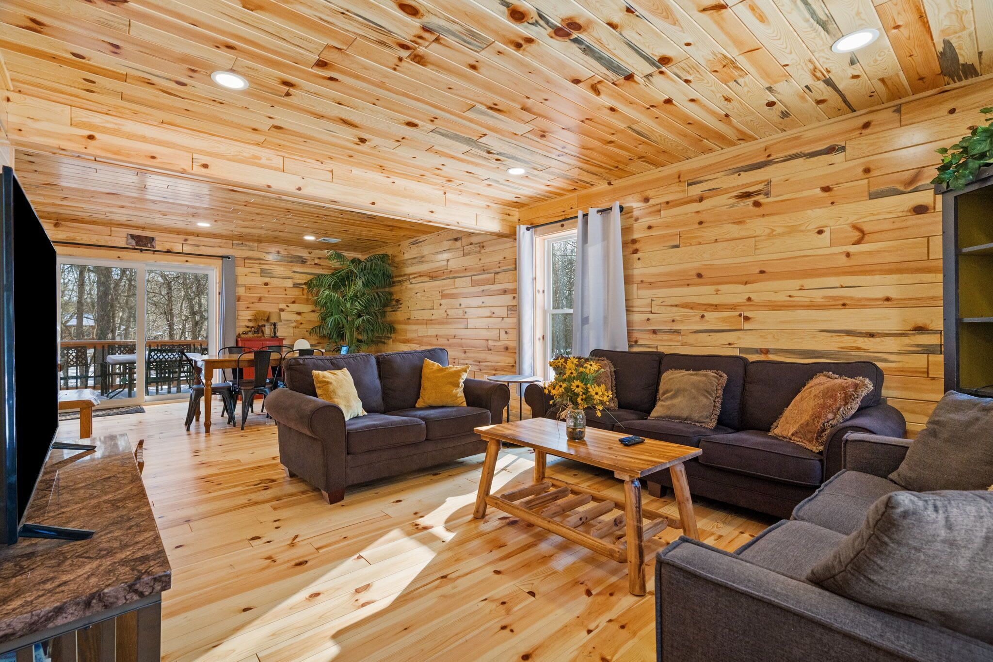 Settle into the cabin living room with plush sofas, a big screen TV, and wooded views beyond the deck