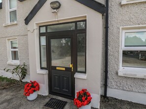 Un bâtiment avec une porte d’entrée noire, deux pots de fleurs rouges et une fenêtre sur le côté droit.
