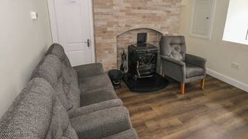 A living room with a brick fireplace, a sofa, a chair, and a clock on the wall.