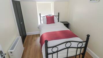 A small, narrow room with a single bed, a bedside table, and a radiator.