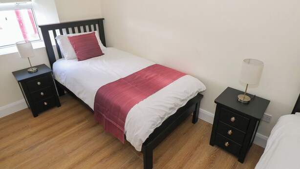 A bedroom with a bed, two bedside tables, a nightstand, a lamp, and a window.