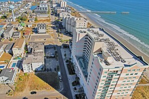 Luftaufnahme einer Küstenstadt mit einem Hotel am Strand, einem Parkplatz und einer Straße.