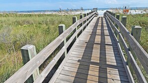 Ein Holzsteg führt zu einem Strand unter blauem Himmel.