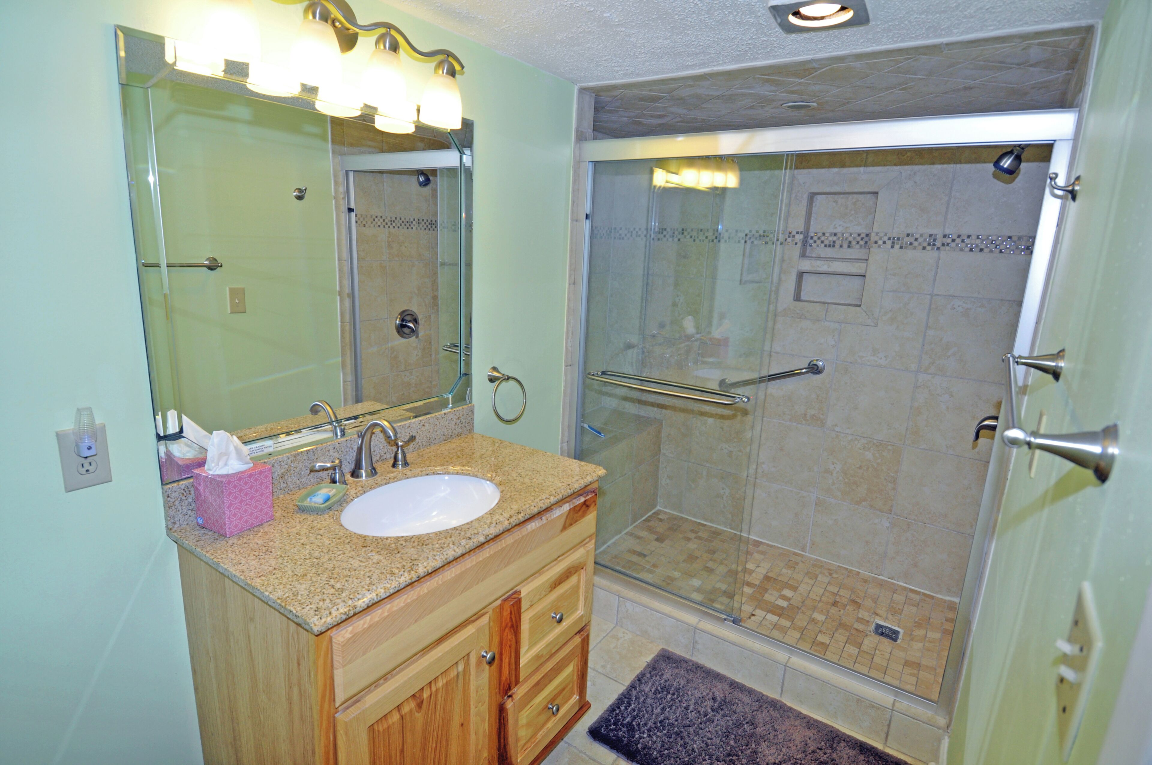 A bathroom with a sink, mirror, vanity, and a glass-enclosed shower area.