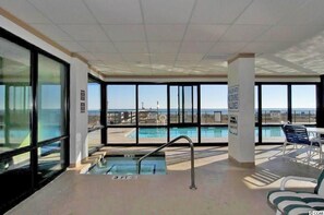 Un espace piscine avec vue sur l’océan, une piscine peu profonde (environ 1 mètre) et un coin salon avec une table et des chaises.
