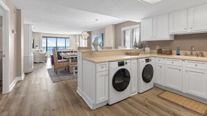 A modern kitchen with built-in appliances, a dining area with a view, and a laundry room. - Oceanfront Luxury 3BR/2BA  End Unit with Pool, Fitness Room and Hot Tubs. (North Myrtle Beach)