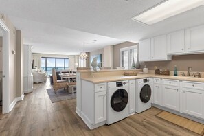 A modern kitchen with built-in appliances, a dining area with a view, and a laundry room. - Oceanfront Luxury 3BR/2BA  End Unit with Pool, Fitness Room and Hot Tubs. (North Myrtle Beach)