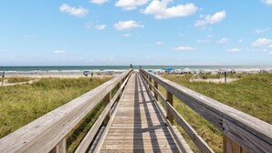 A wooden boardwalk leading to a beach with umbrellas and people. - Oceanfront Luxury 3BR/2BA  End Unit with Pool, Fitness Room and Hot Tubs. (North Myrtle Beach)