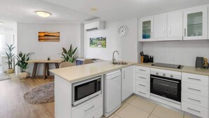 Une cuisine moderne avec des meubles blancs, un four encastré, un micro-ondes et un évier.