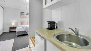 A compact hotel room with a kitchenette, a bed, a bedside table with a lamp, and a painting on the wall. - Peak Studio—Highview Haven across Shopping Centre (Cairns)