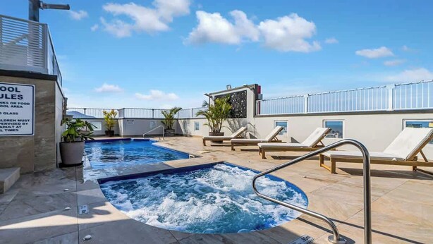 A rooftop pool with lounge chairs, a hot tub, and a sign indicating pool rules. - Peak Studio—Highview Haven across Shopping Centre (Cairns)