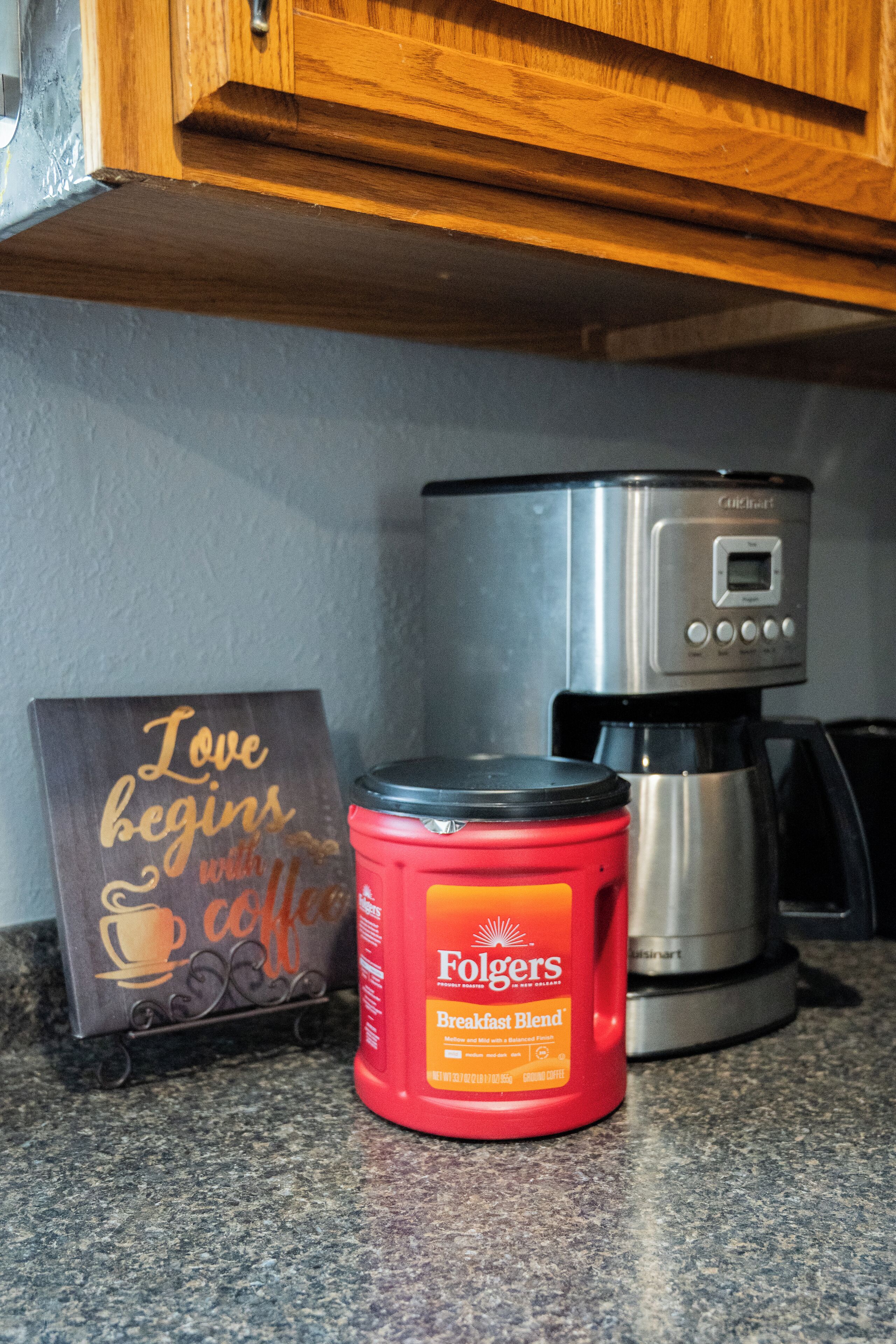 Una encimera de cocina con una cafetera, un tarro rojo de Folgers y un letrero que dice 'El amor comienza con el café'.
