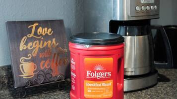 Una encimera de cocina con una cafetera, un tarro rojo de Folgers y un letrero que dice 'El amor comienza con el café'.