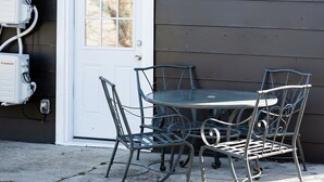 Ein Metall-Gartentisch mit Stühlen, im Hintergrund eine weiße Tür und Stromkästen.
